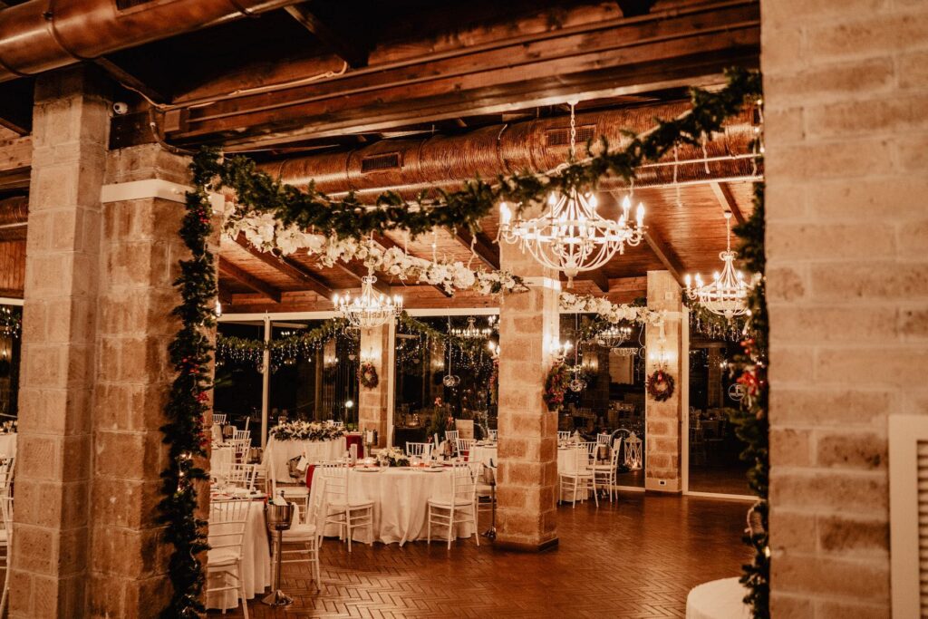 La sala della Tenuta Fabiana addobbata per Natale: lampadari accesi, festoni di verde e tavoli apparecchiati in bianco.
